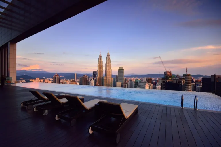 Luxury rooftop infinity pool deck overlooking the Petronas Twin Towers and KL Tower during a purple sunset.