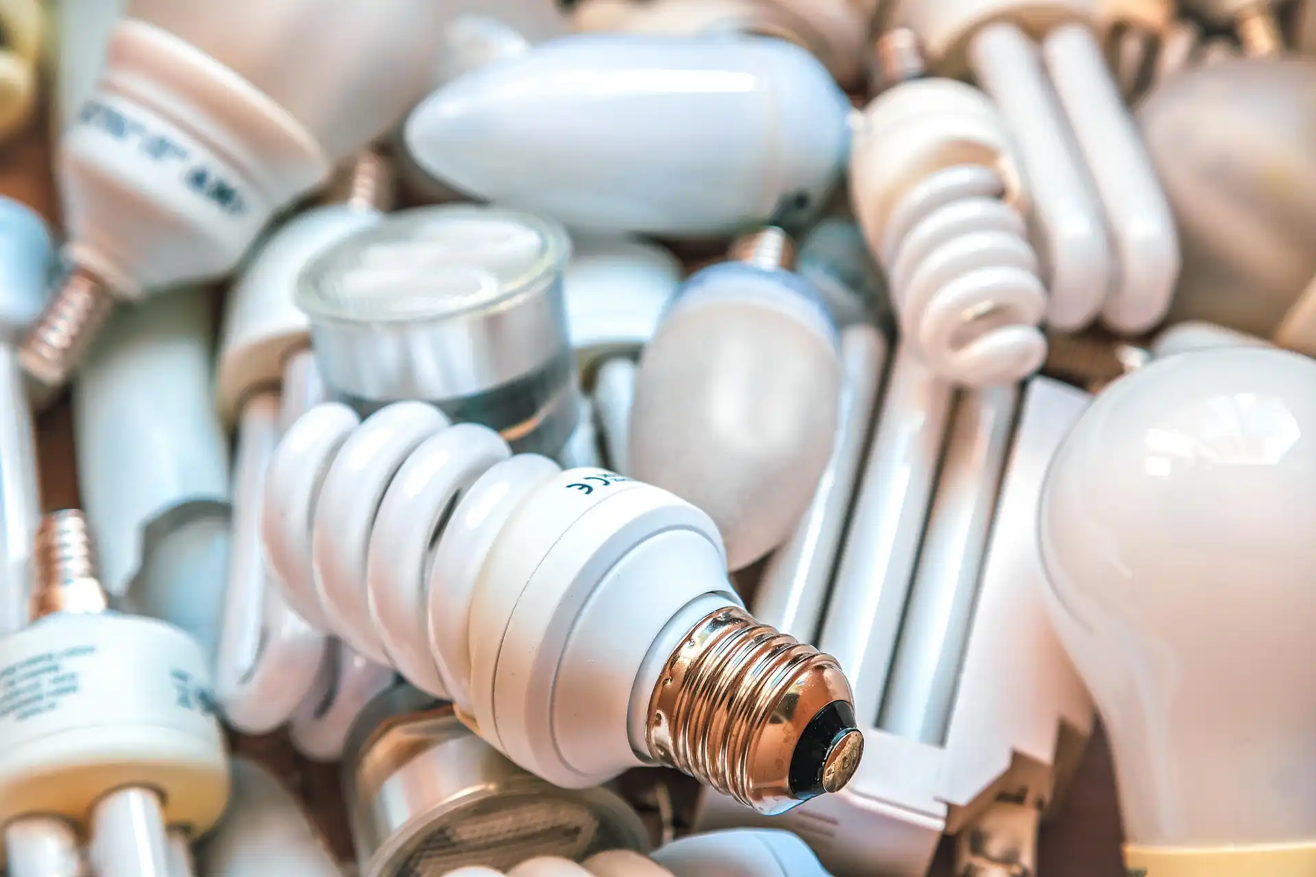 Pile of assorted used light bulbs including LED, CFL, and incandescent types in a close-up view