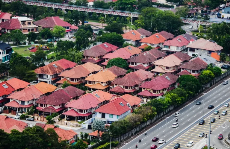 Aerial view of red-roofed terrace houses next to a major highway and MRT track in a Selangor suburb.