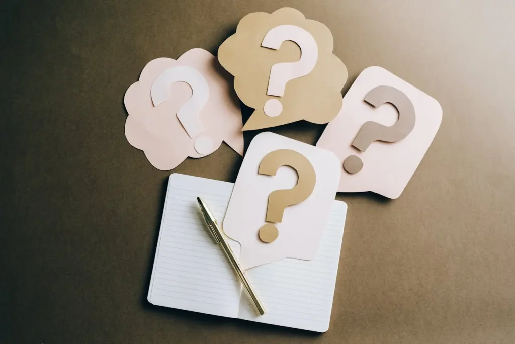 Flat lay of a notebook and pen surrounded by paper cutouts of question marks, representing the checklist of questions for first-time homebuyers in Malaysia.