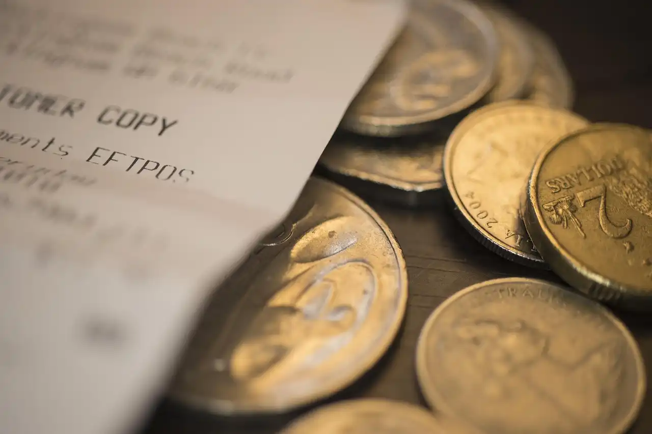 Close-up view of gold and silver coins scattered next to a white printed payment receipt, representing daily household spending.