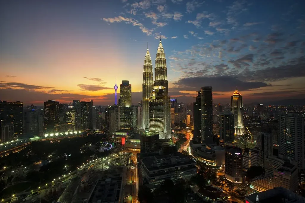 Panoramic night view of the Kuala Lumpur city skyline featuring the glowing Petronas Twin Towers and KL Tower, illustrating prime real estate.