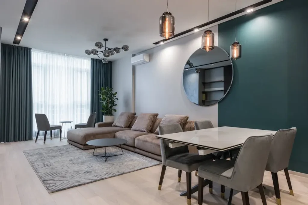 Modern living room interior with grey sofa, round mirror, and dining table, representing a typical serviced apartment unit in Malaysia.