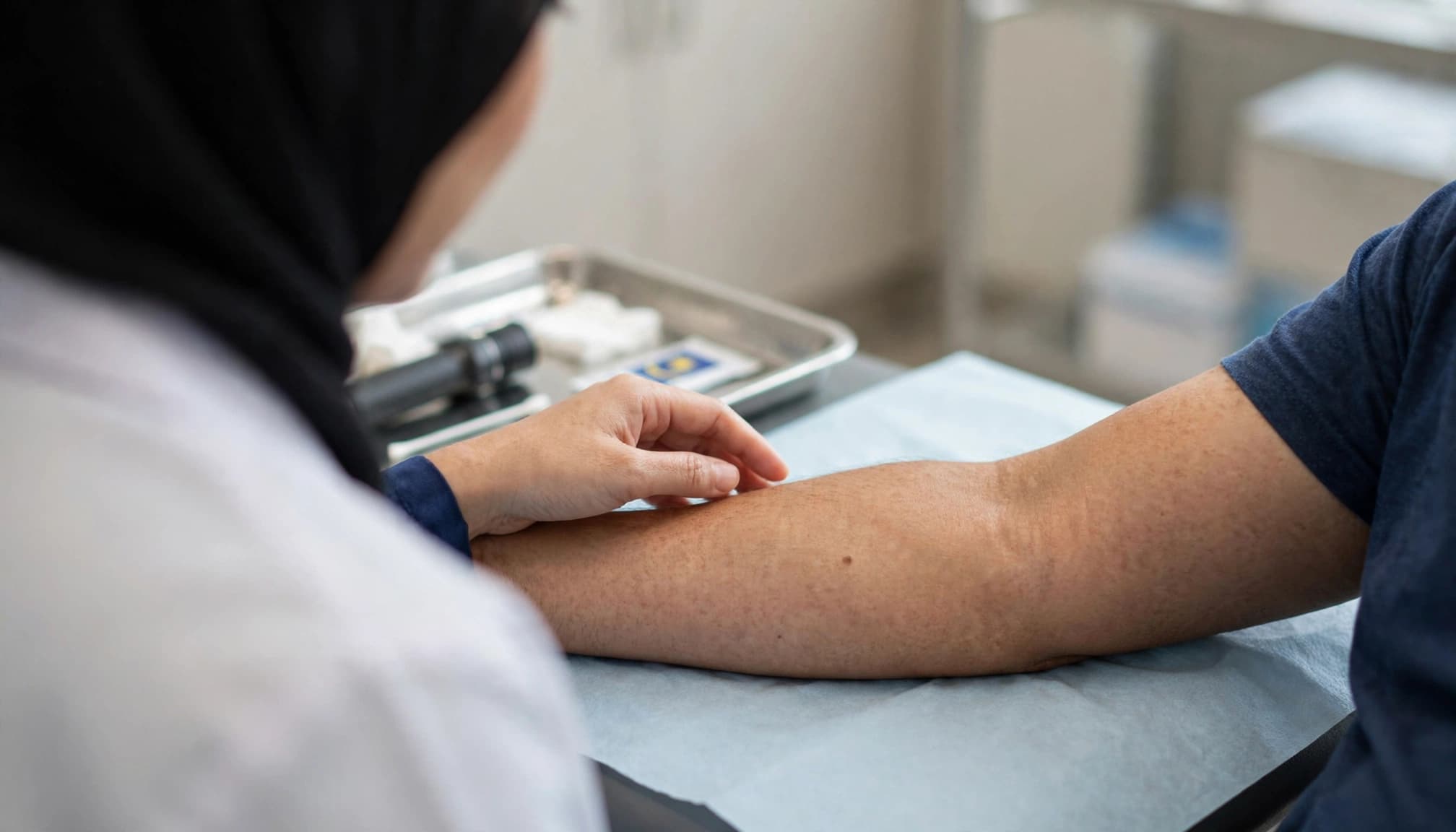 Dermatologist examining a small mole on a patient's forearm in a clean clinic.